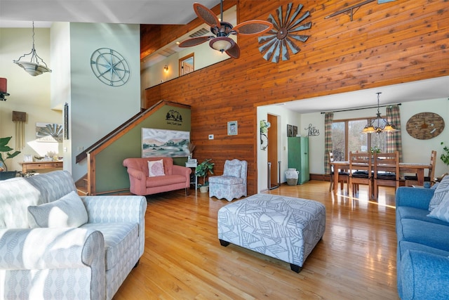 living room with ceiling fan, high vaulted ceiling, wooden walls, and light hardwood / wood-style floors