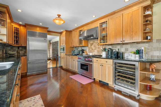 kitchen featuring wine cooler, dark wood-type flooring, wall chimney exhaust hood, built in appliances, and dark stone countertops