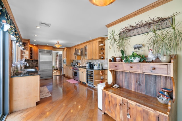 kitchen with wine cooler, built in appliances, decorative backsplash, and wall chimney range hood