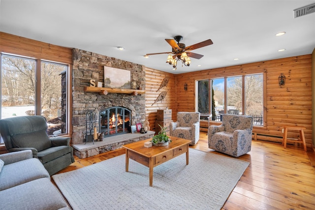 living room with ceiling fan, a stone fireplace, rustic walls, and light hardwood / wood-style floors