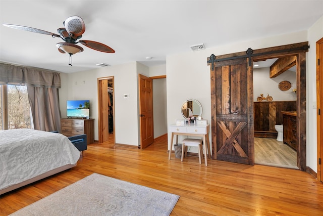 bedroom with a walk in closet, a barn door, connected bathroom, and light wood-type flooring