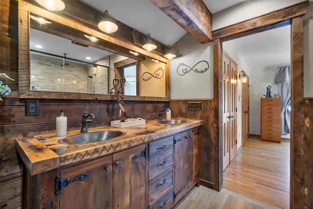 bathroom with wood walls, a shower with shower door, wood-type flooring, vanity, and beam ceiling