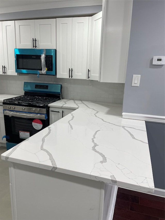 kitchen featuring light stone counters, stainless steel range with gas stovetop, and white cabinets