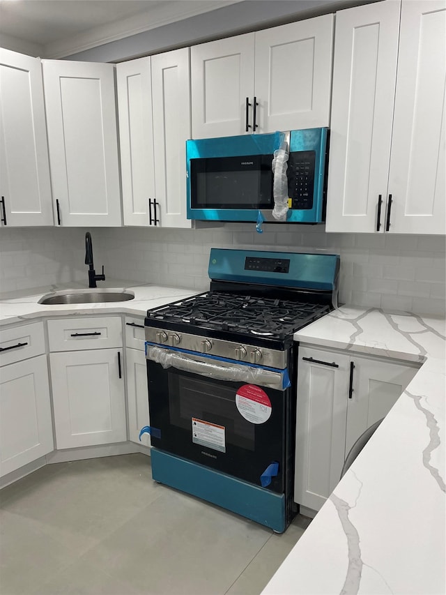 kitchen with gas stove, light stone countertops, sink, and white cabinets