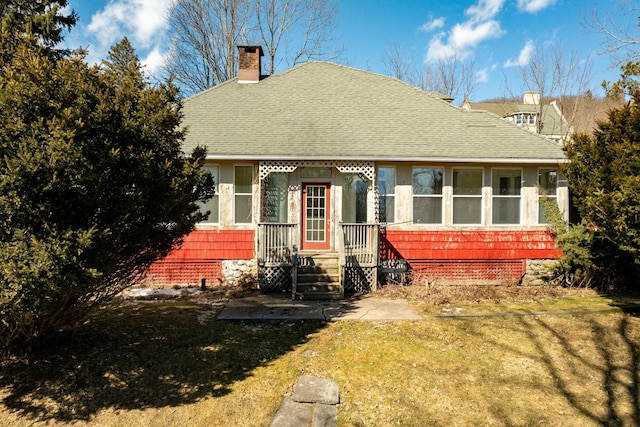 view of front of property featuring a shingled roof, a chimney, and a front lawn