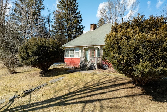 view of front facade with a front lawn, a chimney, and a shingled roof