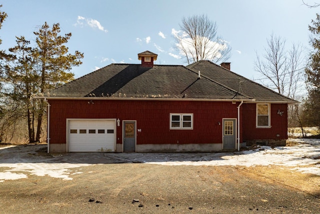 view of side of property featuring a shingled roof, driveway, a chimney, and an attached garage