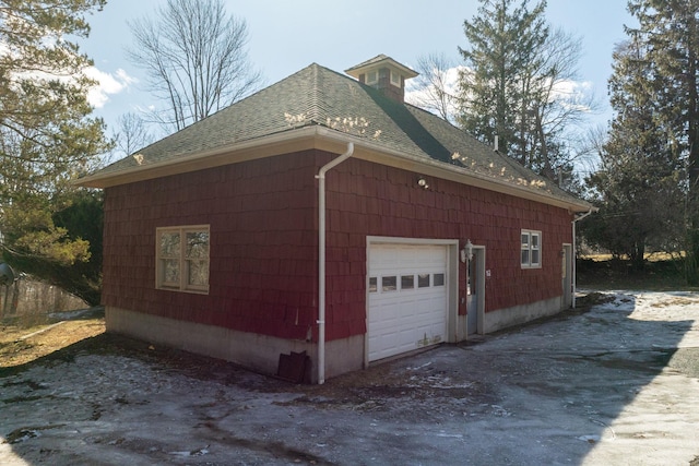 view of side of home featuring driveway, a shingled roof, and a garage