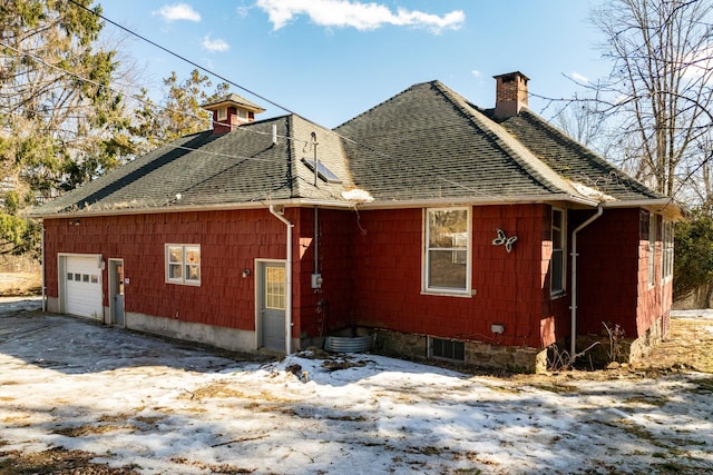 view of home's exterior with an attached garage, a shingled roof, and a chimney