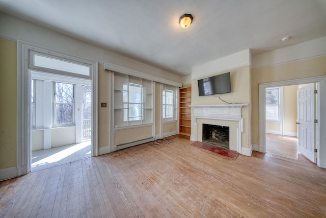 unfurnished living room with a baseboard heating unit, a wealth of natural light, a fireplace, and light wood-style floors