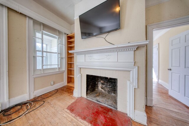 unfurnished living room with built in shelves, a fireplace, baseboards, and hardwood / wood-style floors