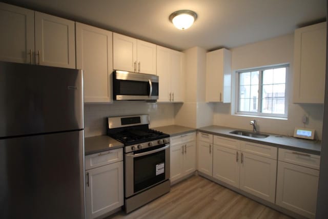 kitchen with sink, appliances with stainless steel finishes, white cabinetry, tasteful backsplash, and light wood-type flooring