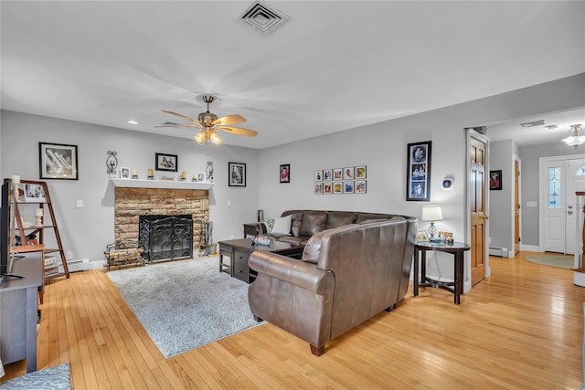 living room featuring a baseboard heating unit, a stone fireplace, light hardwood / wood-style floors, and ceiling fan