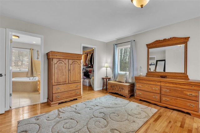 bedroom with ensuite bath, a spacious closet, light hardwood / wood-style floors, and a closet