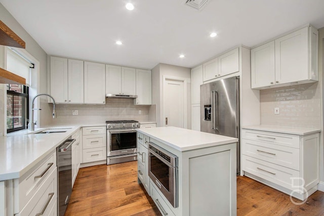 kitchen with high end appliances, sink, a kitchen island, and white cabinets