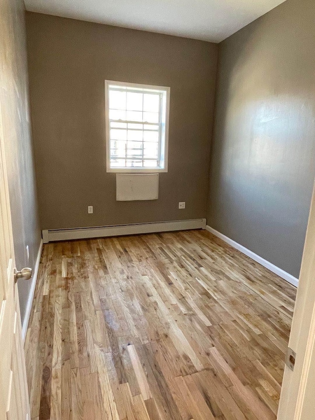 unfurnished room with a baseboard heating unit and light hardwood / wood-style flooring