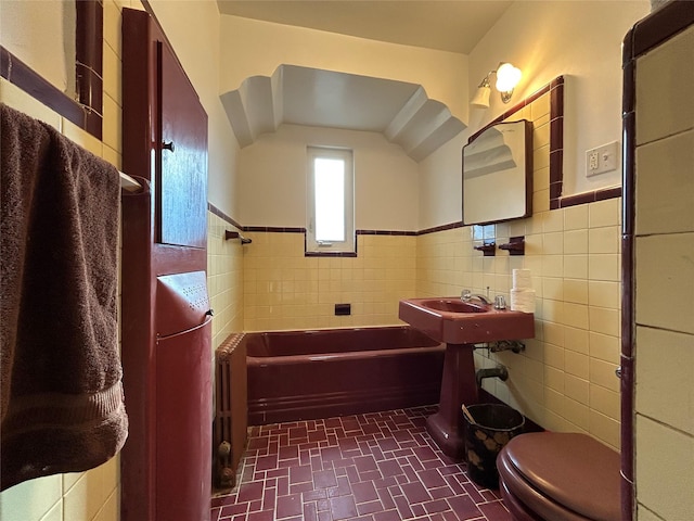 bathroom with toilet, sink, tile walls, and a washtub