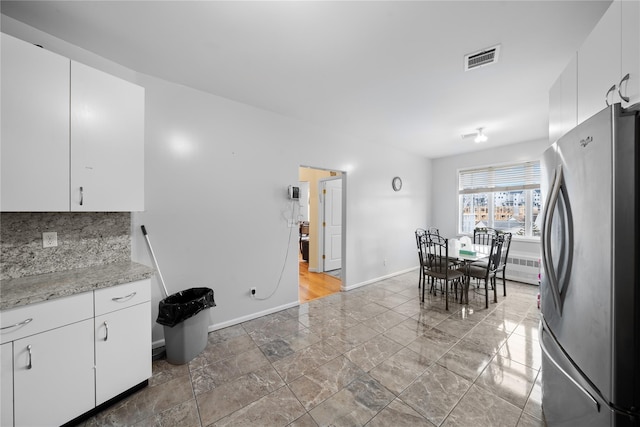 kitchen with white cabinetry, light stone counters, decorative backsplash, and stainless steel refrigerator