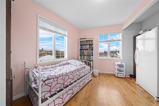 bedroom featuring white refrigerator, multiple windows, and light wood-type flooring