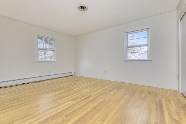 empty room with a baseboard heating unit, a wealth of natural light, and light hardwood / wood-style flooring