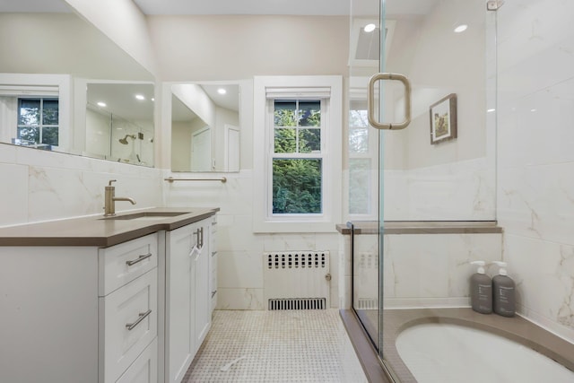 bathroom with a shower with door, vanity, radiator, and tile walls