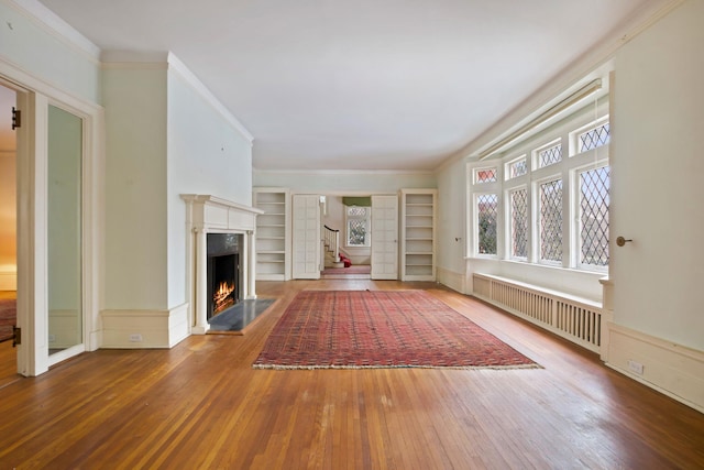 unfurnished living room featuring hardwood / wood-style flooring, ornamental molding, radiator, and built in features