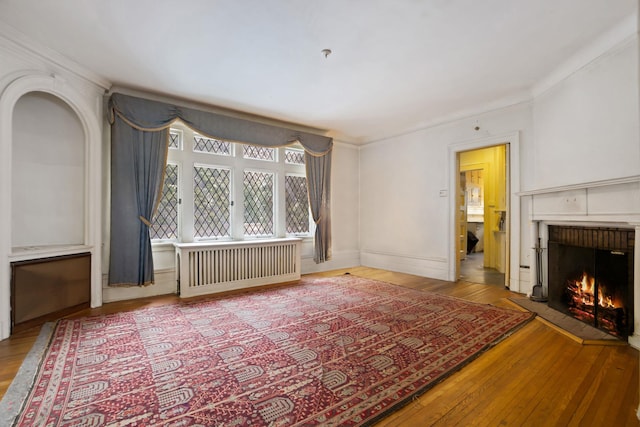 unfurnished living room with hardwood / wood-style flooring, ornamental molding, a brick fireplace, and radiator heating unit