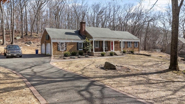 view of front facade with driveway, covered porch, a garage, and a chimney