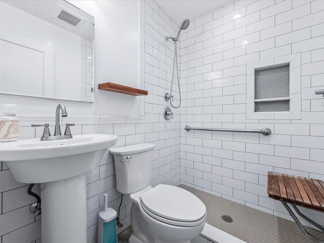 bathroom with tile walls, sink, toilet, and tiled shower