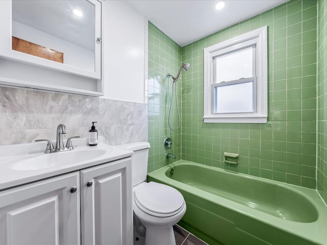 full bathroom with tile walls, decorative backsplash, tiled shower / bath combo, vanity, and toilet