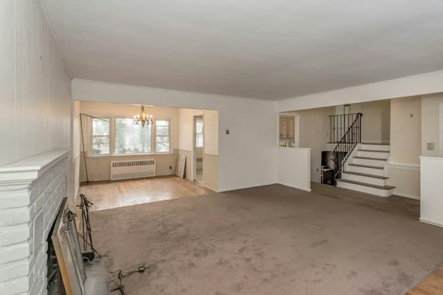 unfurnished living room featuring wood-type flooring, radiator, a notable chandelier, and a fireplace