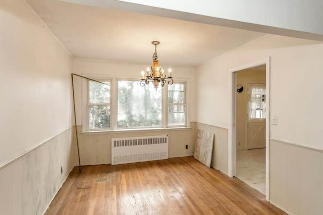 unfurnished dining area with wood-type flooring, radiator, and a notable chandelier