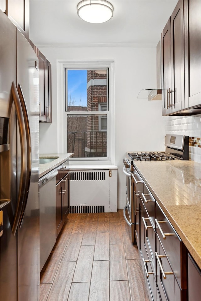 kitchen with appliances with stainless steel finishes, radiator heating unit, backsplash, dark brown cabinetry, and light wood-type flooring