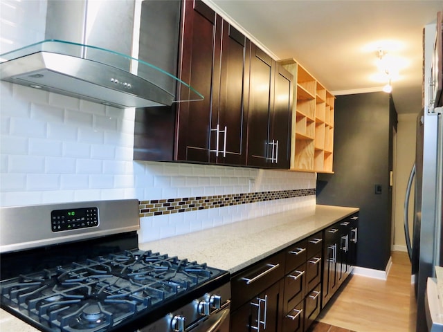 kitchen featuring backsplash, island exhaust hood, black fridge, stainless steel gas range oven, and light stone countertops