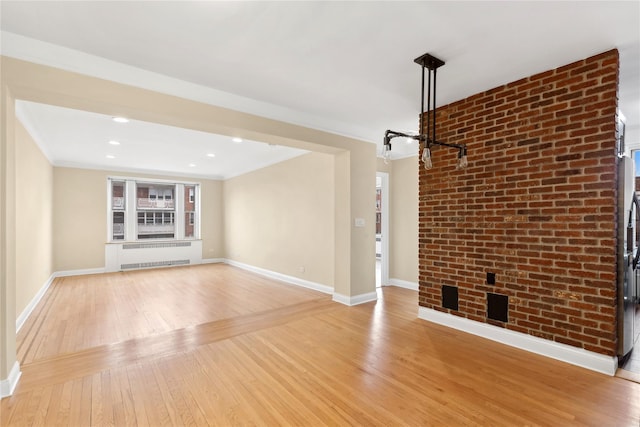 unfurnished living room with radiator, crown molding, brick wall, and light wood-type flooring