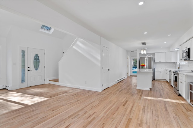 kitchen with a kitchen island, appliances with stainless steel finishes, white cabinets, hanging light fixtures, and a baseboard heating unit