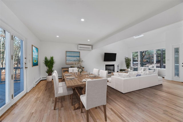 dining room featuring baseboard heating, a wall mounted air conditioner, a healthy amount of sunlight, and light wood-type flooring