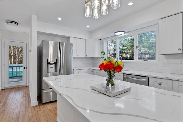 kitchen with hanging light fixtures, light stone countertops, white cabinets, and appliances with stainless steel finishes