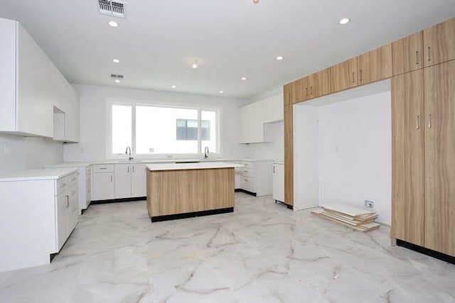 kitchen with recessed lighting, a sink, visible vents, marble finish floor, and a center island