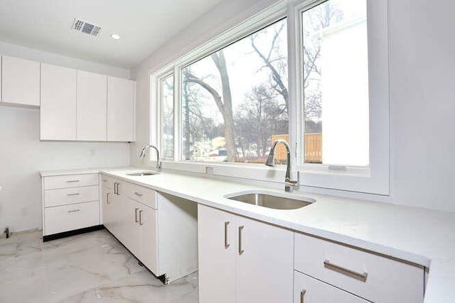 kitchen with a sink, visible vents, white cabinets, marble finish floor, and light countertops