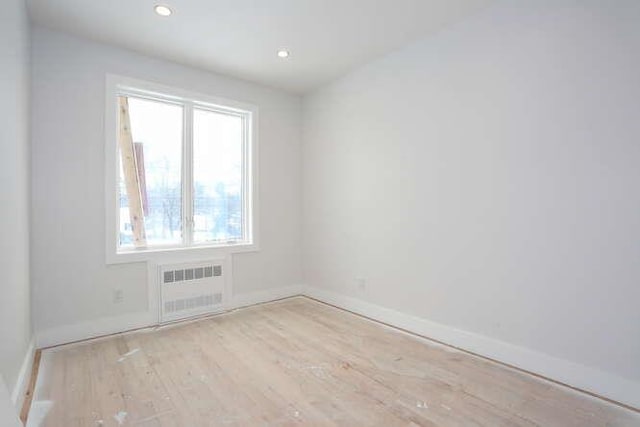 empty room with radiator heating unit, baseboards, wood finished floors, and recessed lighting