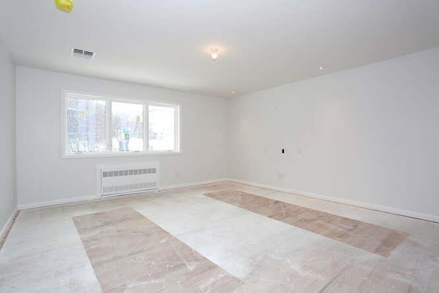 spare room featuring radiator heating unit, visible vents, and baseboards