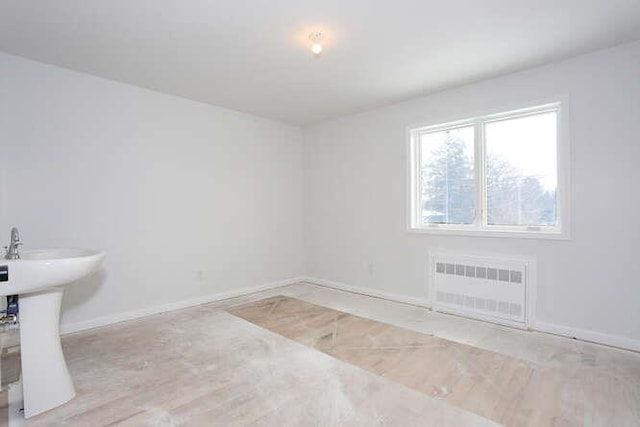 spare room with baseboards, a sink, wood finished floors, and radiator