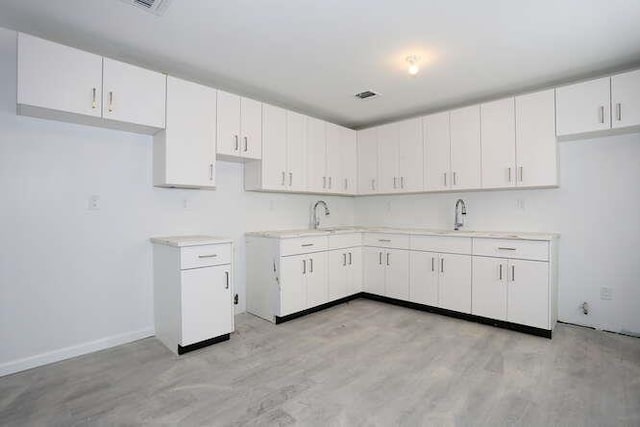 kitchen featuring light wood-style flooring, white cabinetry, light countertops, and a sink