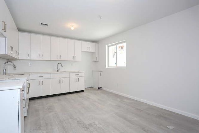 kitchen featuring light wood-type flooring, baseboards, white cabinets, and a sink