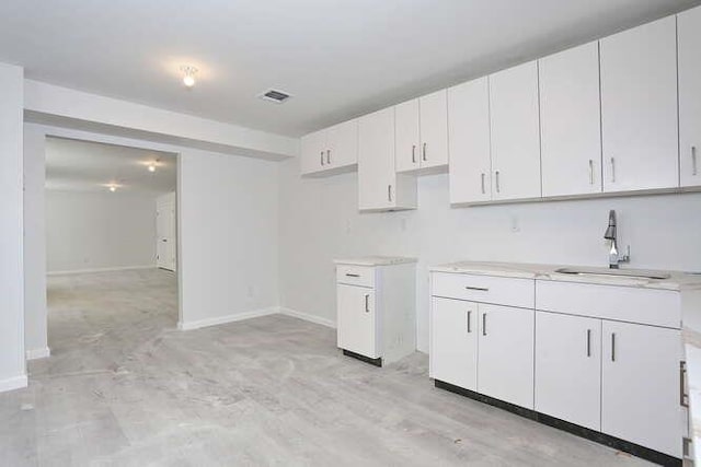 kitchen with light countertops, white cabinets, a sink, and baseboards