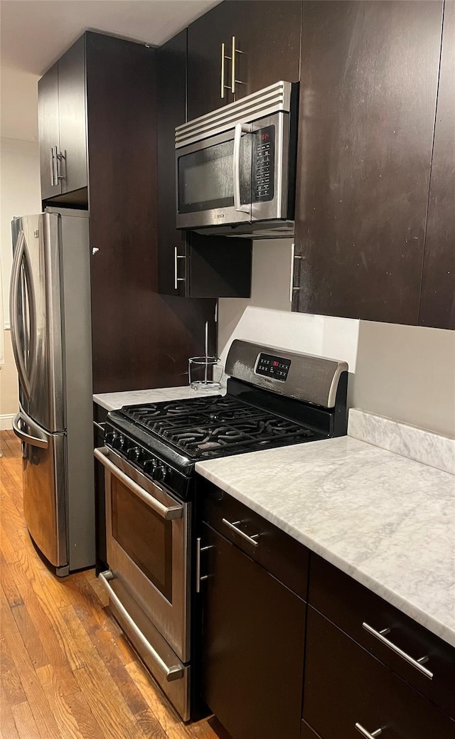 kitchen featuring stainless steel appliances, light stone countertops, and light wood-type flooring