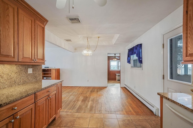 kitchen featuring light stone counters, hanging light fixtures, a baseboard heating unit, ceiling fan, and backsplash