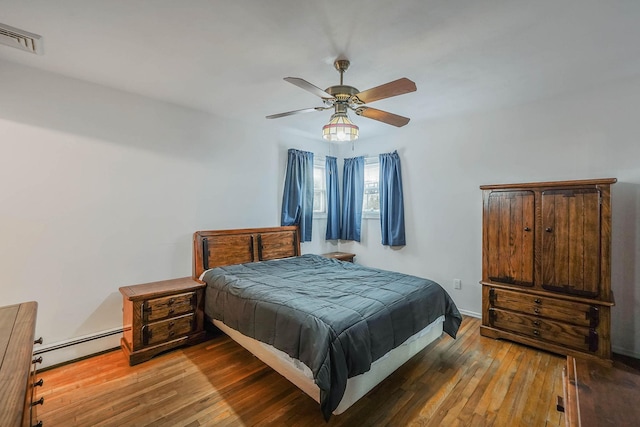 bedroom with a baseboard heating unit, hardwood / wood-style floors, and ceiling fan