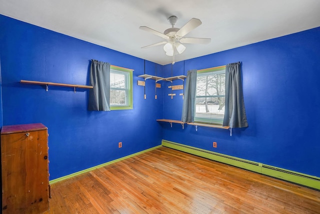 unfurnished bedroom with multiple windows, a baseboard heating unit, hardwood / wood-style floors, and ceiling fan